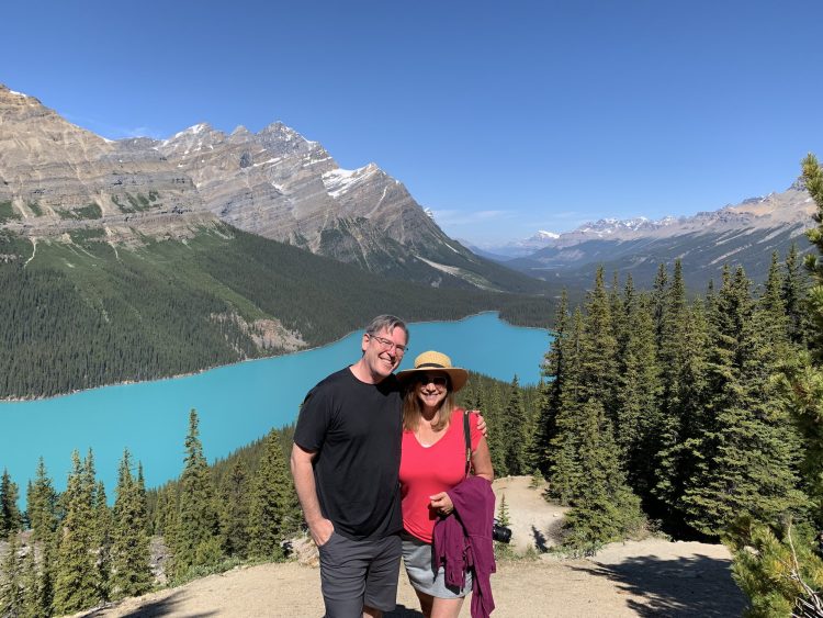 Middle aged couple traveling in Canadian Rockies, posing for photo by beautiful Peyto Lake in Banff