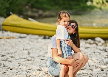 Mother with daughter against canoe in rocky shore of a calm river